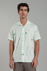 Man wearing a light green shirt with embroidered designs on a gray background